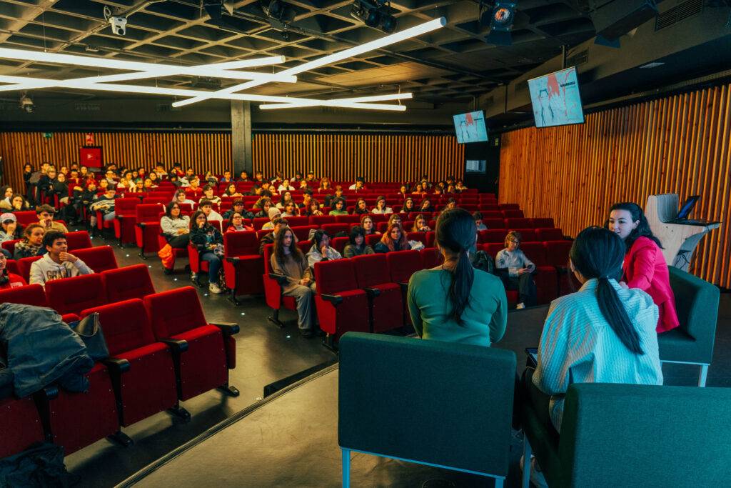 Una charla en un auditorio con varias personas sentadas y dos ponentes en el escenario.