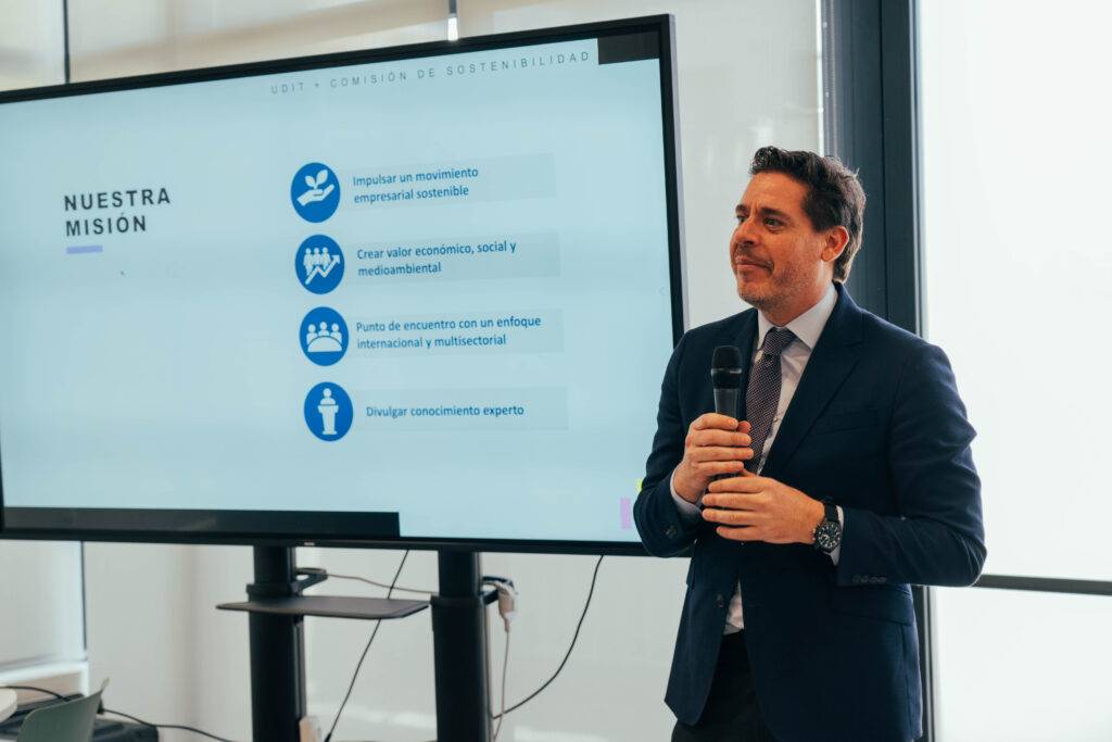 Un hombre presenta una charla sobre una misión empresarial mientras se proyecta información en una pantalla.