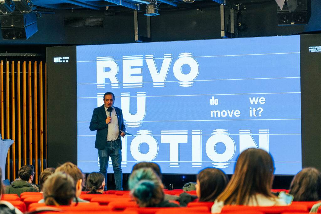 Un hombre da una charla frente a una pantalla con el texto 'REVOLUTION do we move it?'.