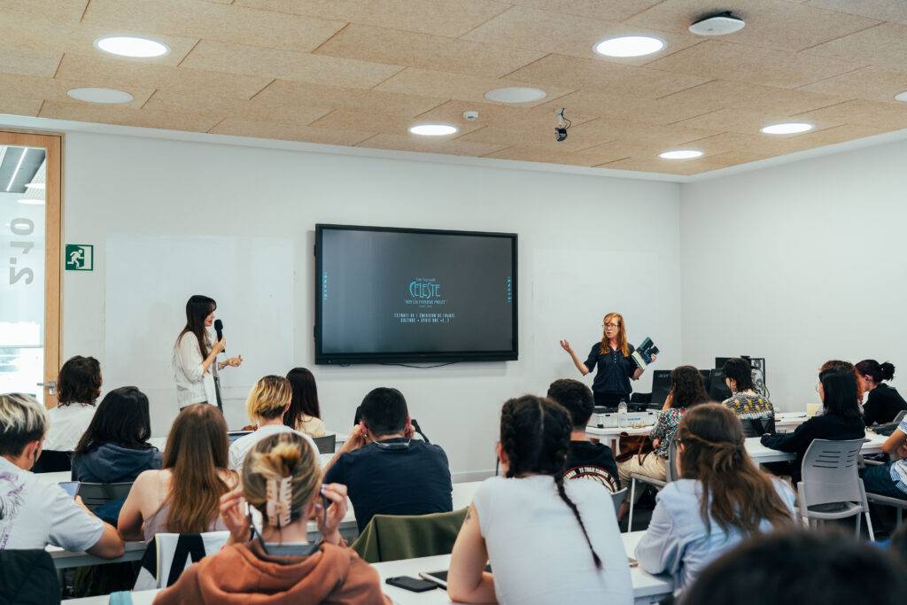 Una presentación en un aula donde dos mujeres hablan frente a un grupo de personas sentadas.