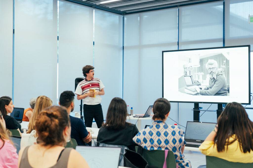 Una persona presenta un tema ante un grupo en una sala con pantallas.