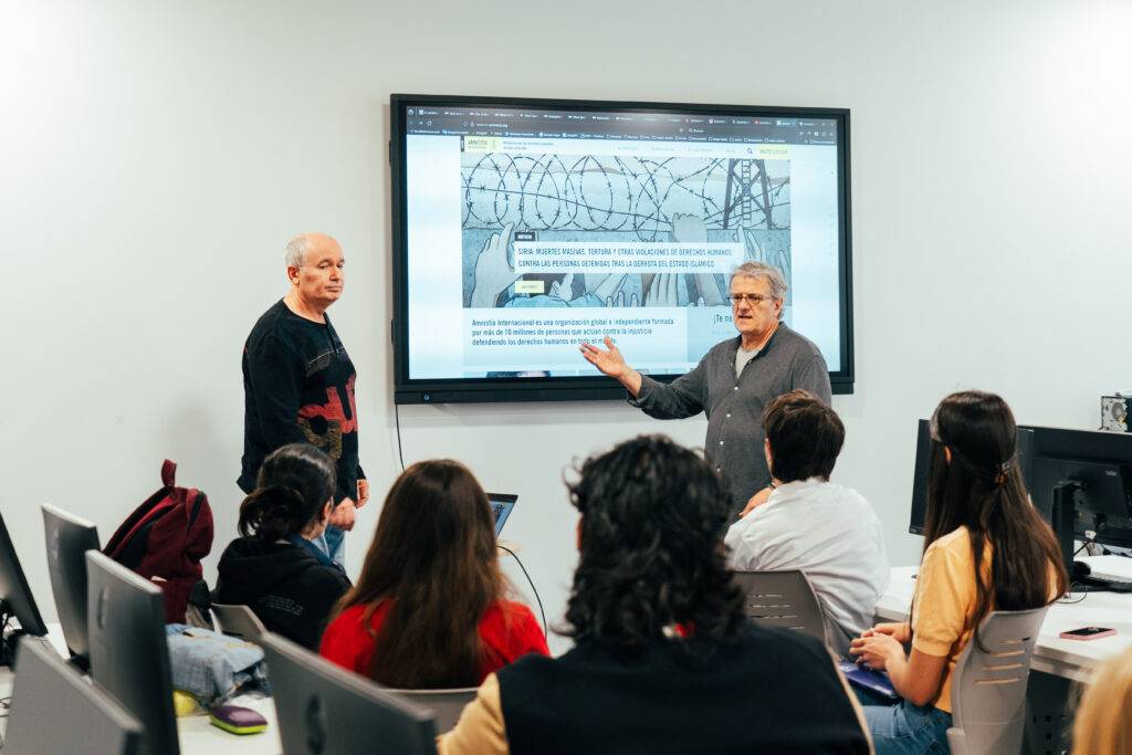 Un grupo de personas asiste a una presentación con dos ponentes en un aula moderna.
