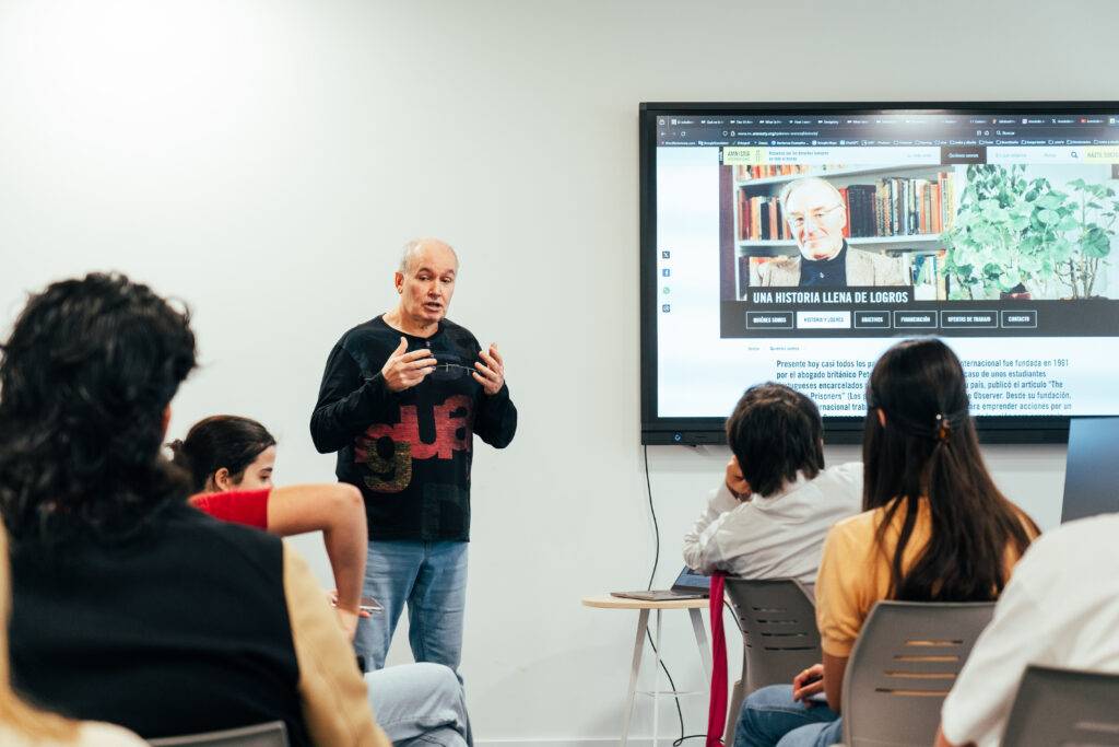 Un hombre está dando una charla frente a un grupo de personas mientras se proyecta una imagen en una pantalla.