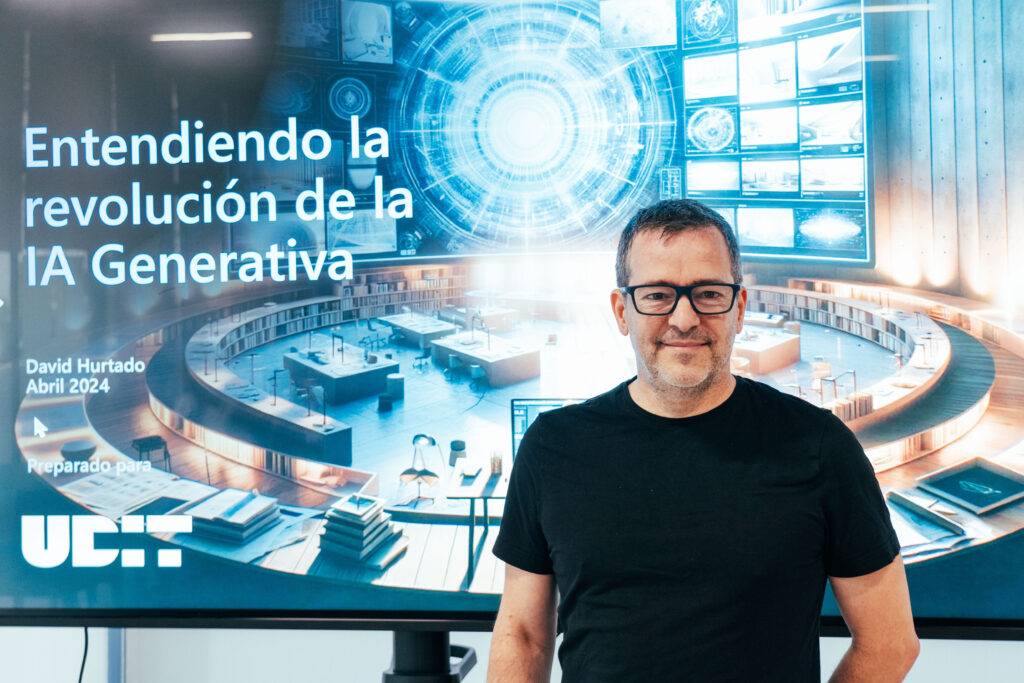 Un hombre posando frente a una pantalla que muestra una presentación sobre la IA Generativa.