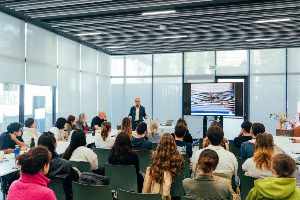 Un grupo de personas presta atención a un ponente que está hablando en una sala iluminada.