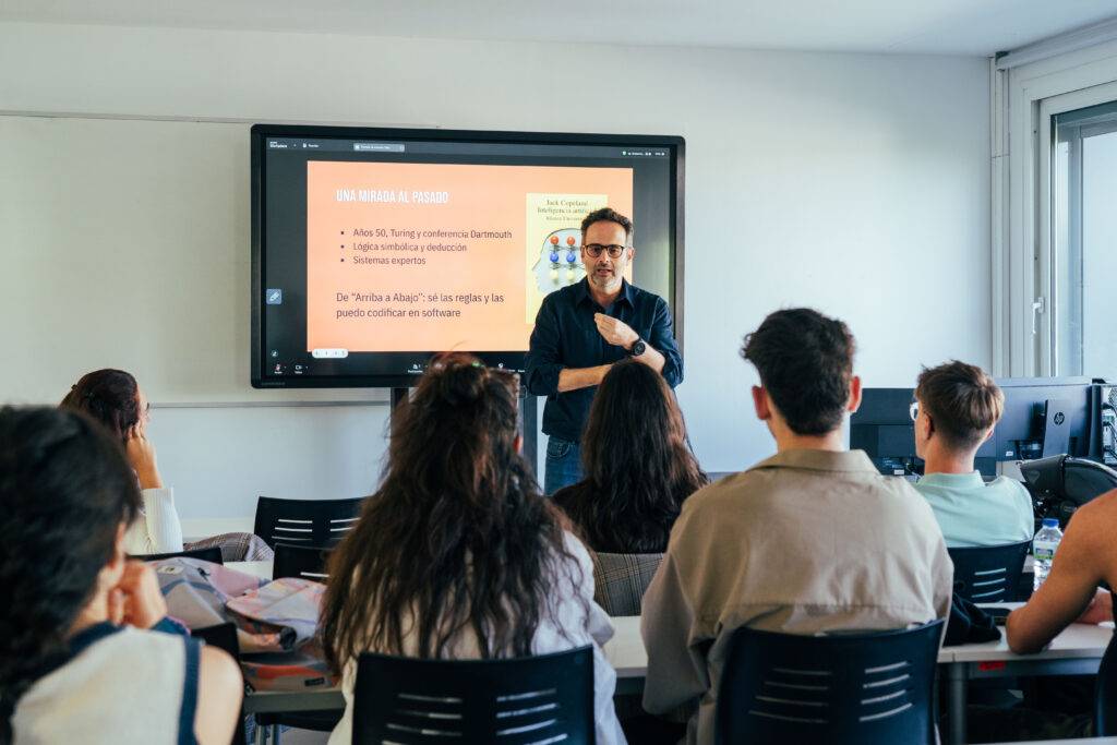 Un profesor está dando una clase frente a un grupo de estudiantes en un aula moderna.