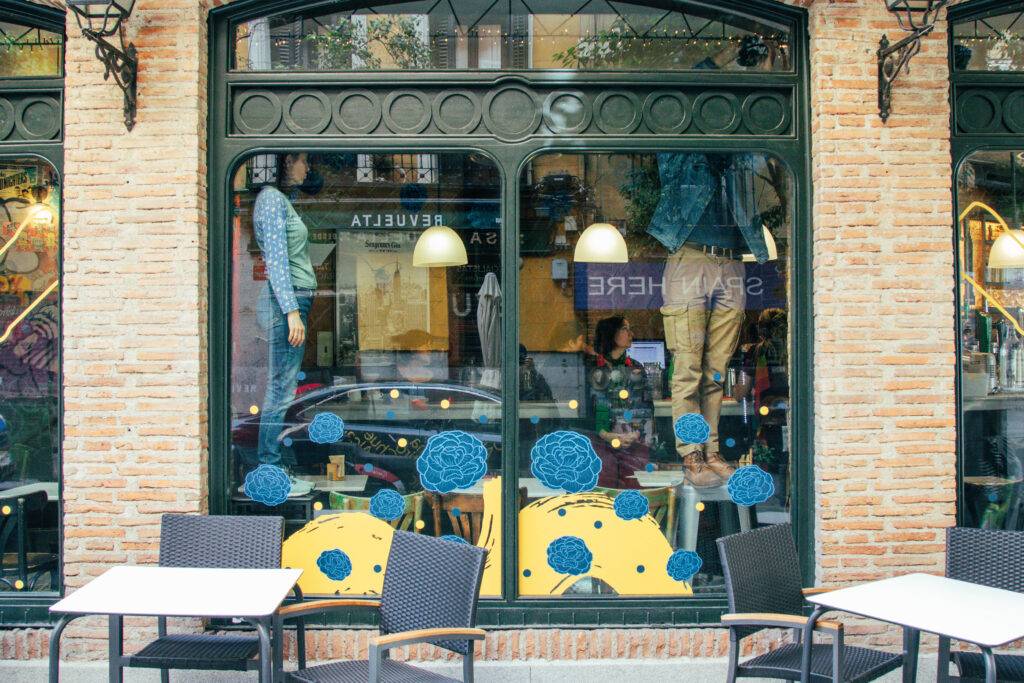 Una vitrina de tienda con maniquíes vestidos y una decoración colorida en las ventanas.