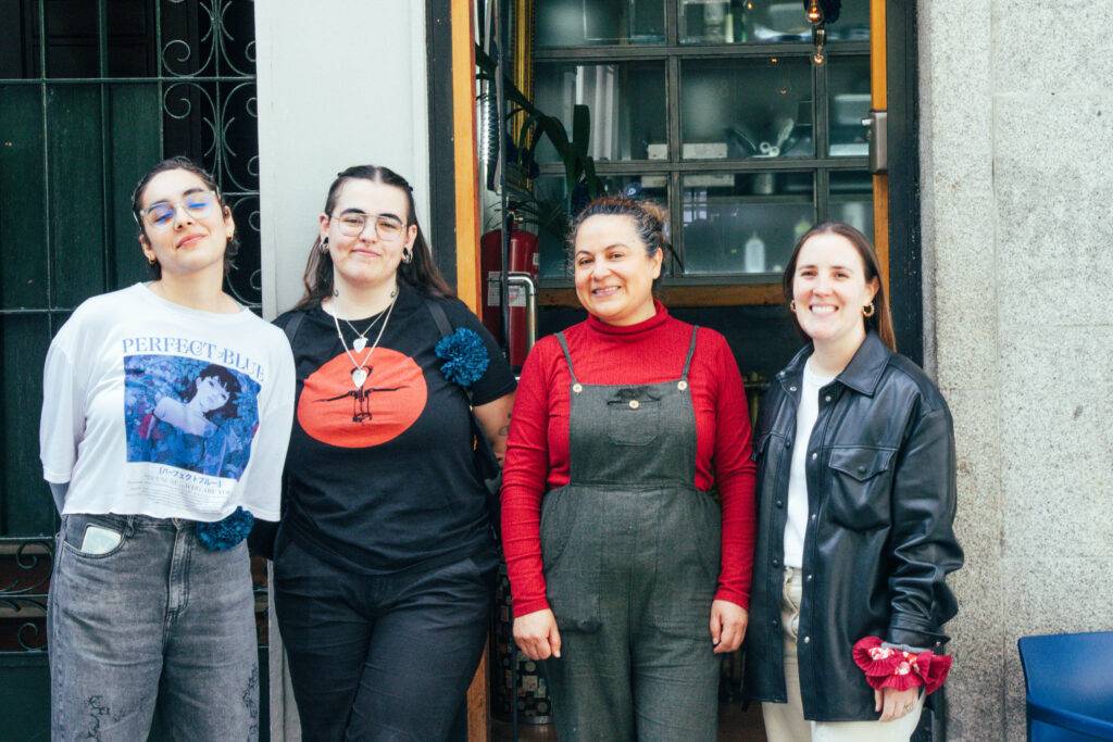 Cuatro mujeres posan juntas frente a una entrada, mostrando un ambiente amigable y contemporáneo.