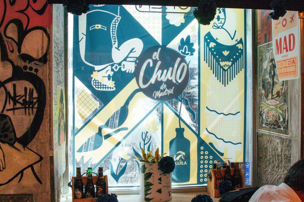 Una ventana decorada con arte colorido y el logotipo de un establecimiento llamado 'el Chulo de Madrid'.