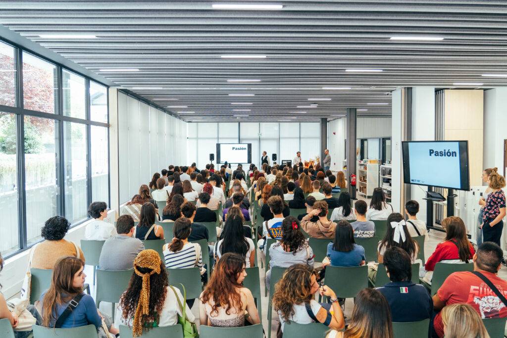 La imagen muestra a un gran grupo de personas sentadas en un auditorio asistiendo a una presentación.