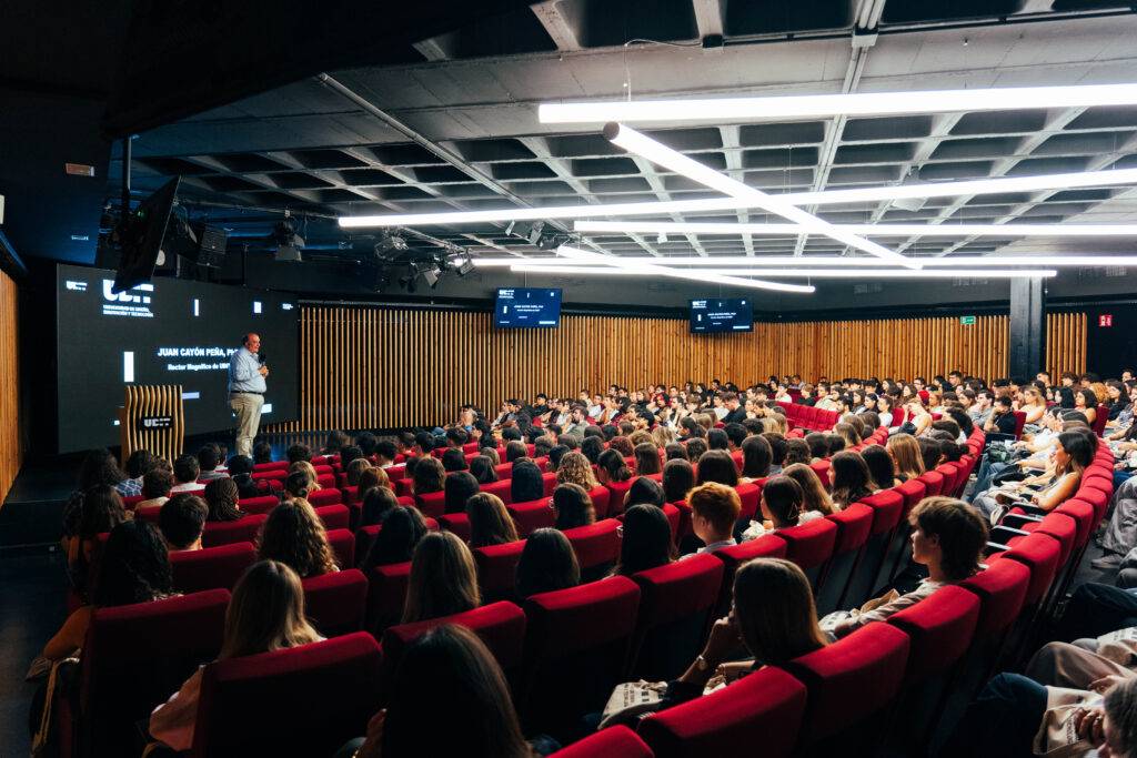 Una conferencia con un orador y una audiencia numerosa en un auditorio moderno.