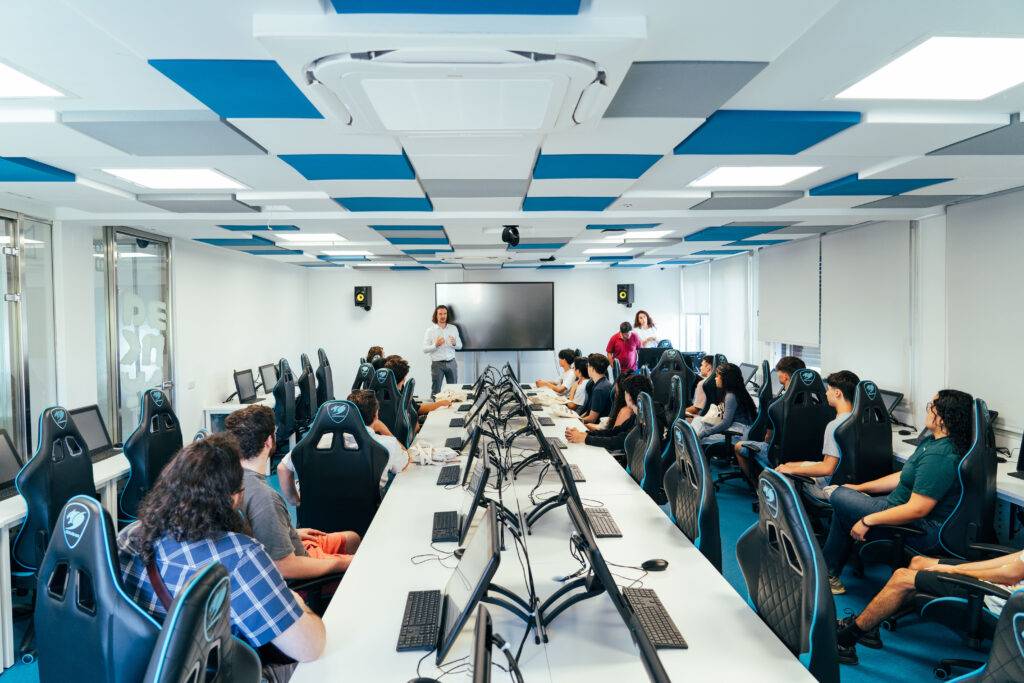 Una sala de capacitación equipada con computadoras y asientos ergonómicos, donde un grupo de personas asiste a una presentación.
