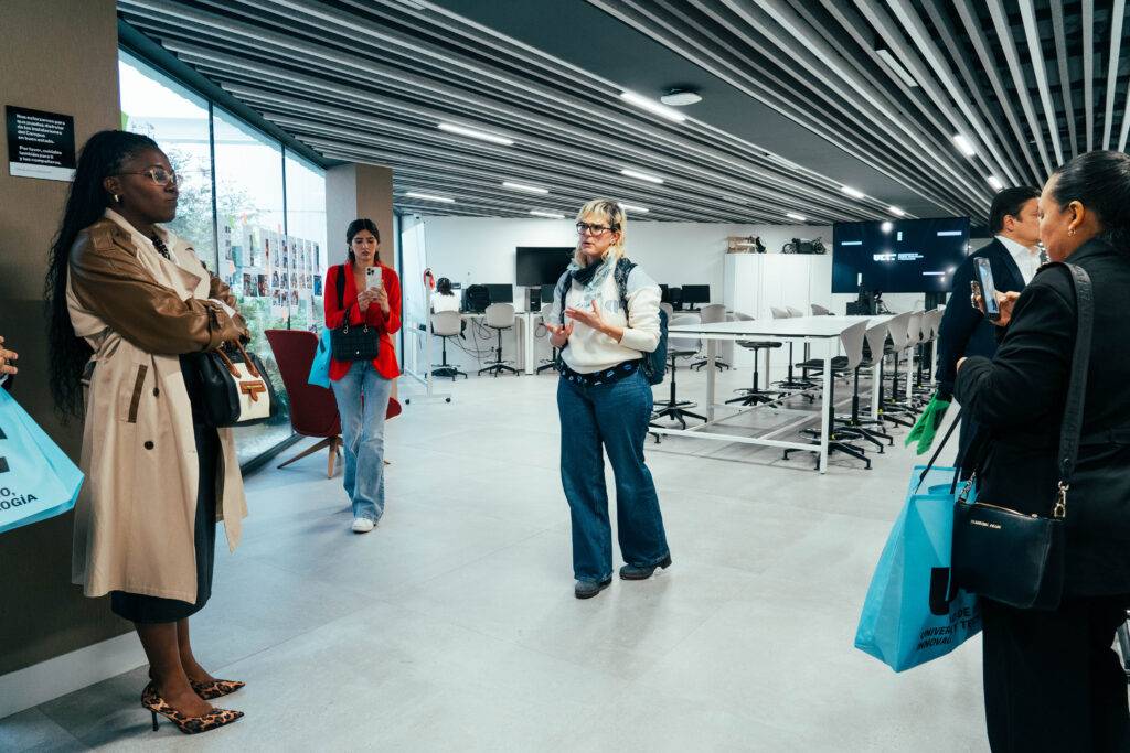 Un grupo de personas escucha atentamente a una mujer que está hablando en un espacio moderno y bien iluminado.