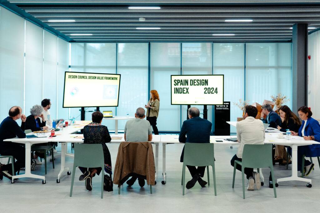 Una reunión de diseño en un espacio moderno con un presentador y varios participantes atentos.