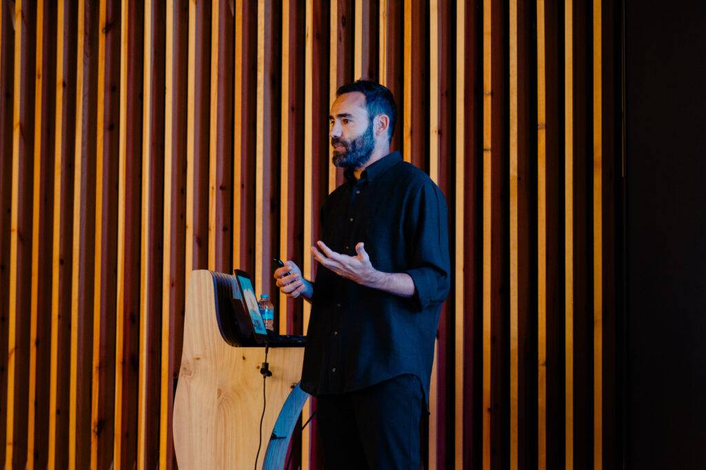 Un hombre está haciendo una presentación frente a un panel de madera.