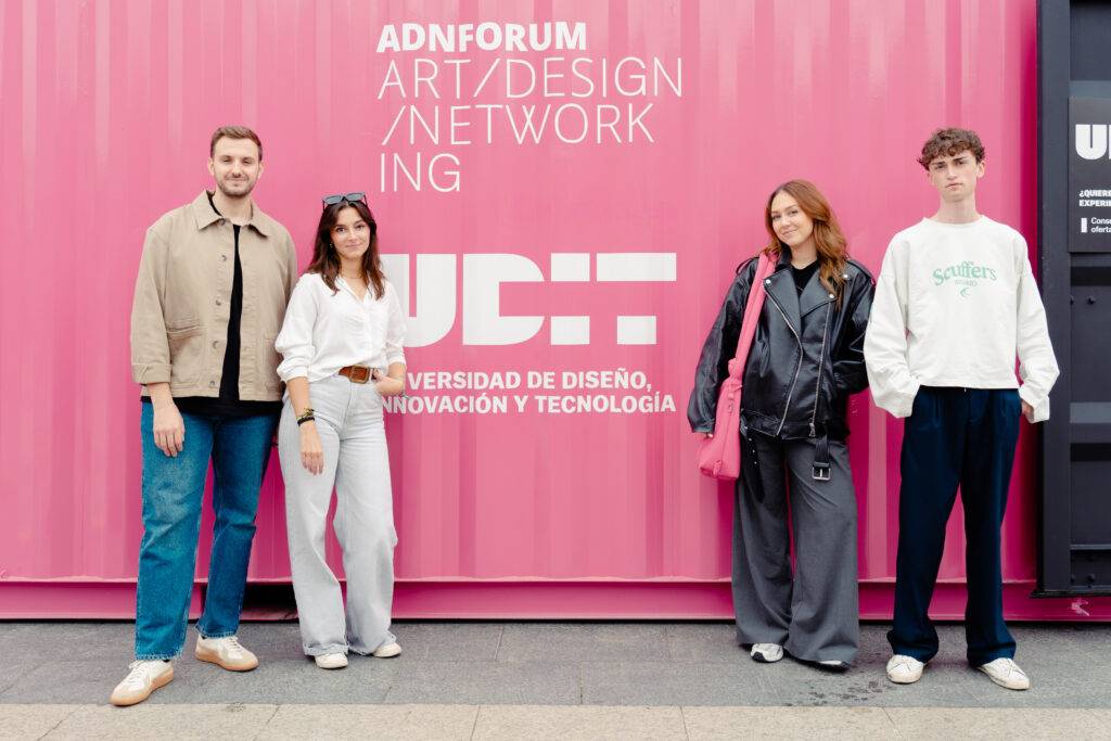 Cuatro personas posan frente a un contenedor rosa con el logo de un evento de diseño y tecnología.