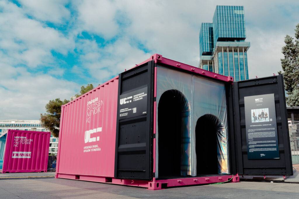 Un contenedor rosa con ventanas oscuras se exhibe en un espacio urbano contemporáneo.