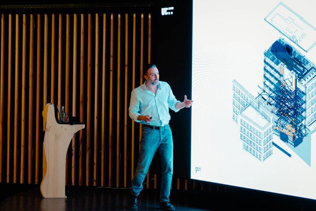 Un hombre presenta un proyecto arquitectónico frente a una pantalla en un evento.