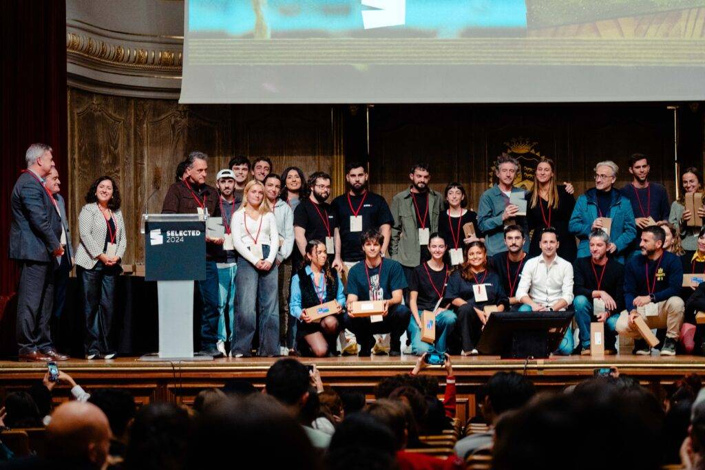 Un grupo de personas posando en un evento con un escenario y un cartel en el fondo.