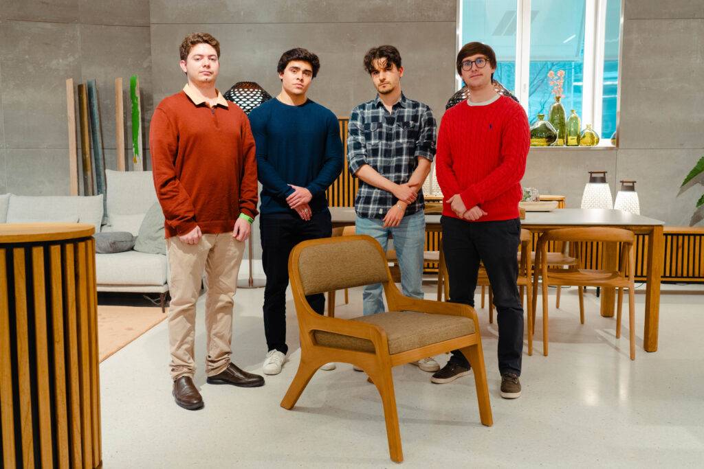 Cuatro jóvenes posan frente a una silla de diseño moderno en un ambiente minimalista.