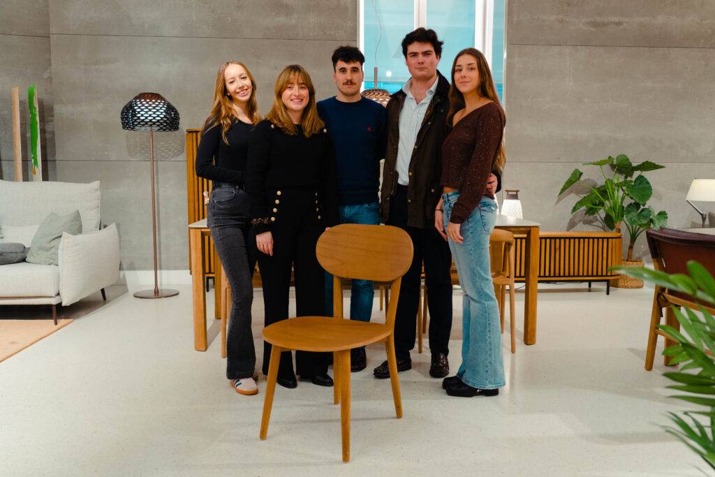 Un grupo de cinco personas posa junto a una silla en un ambiente moderno y acogedor.
