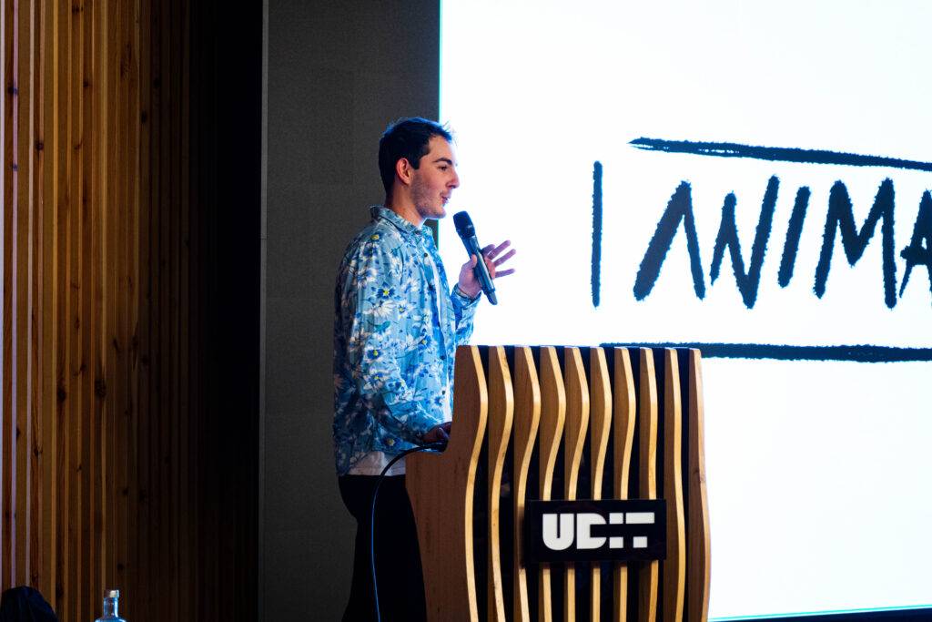 Un joven presentador habla frente a una pantalla grande con la palabra 'ANIMAL'.