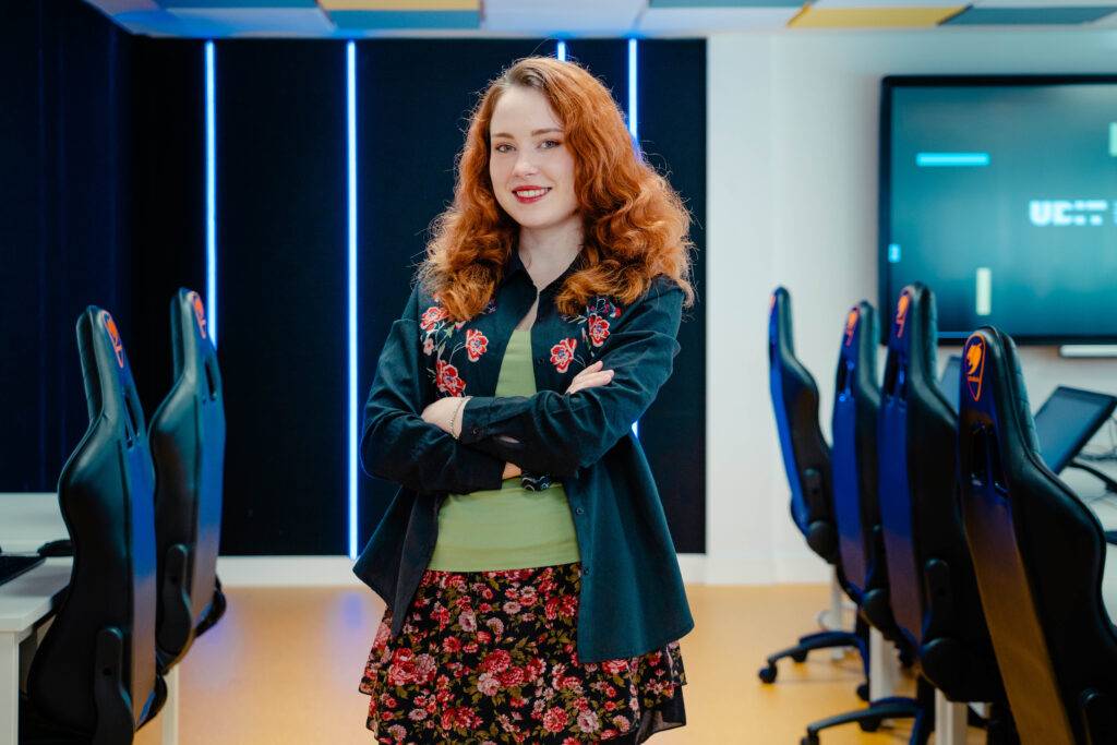 Una joven con cabello rizado y pelirrojo sonríe en un aula moderna de computación.