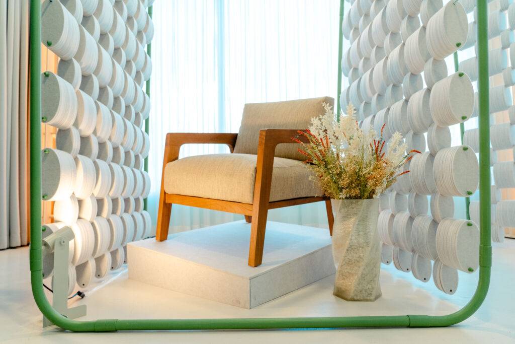 Una silla de diseño moderno con un jarrón de flores, enmarcada por una estructura de tubos color verde y rodeada de cortinas.
