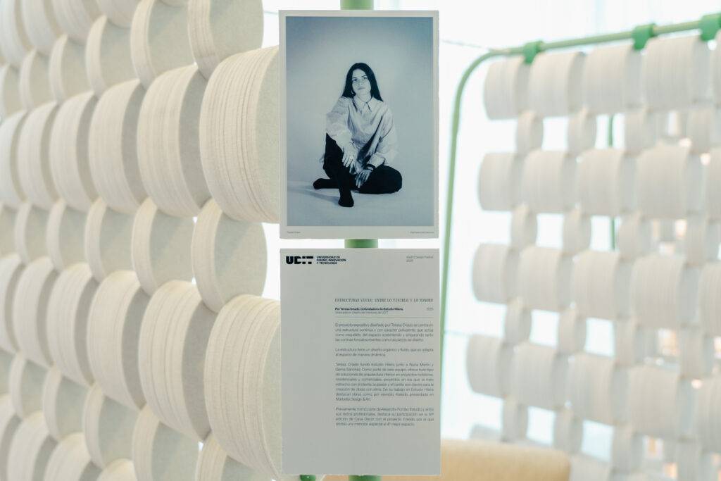 Una persona sentada en una exposición artística, rodeada de elementos decorativos en blanco.