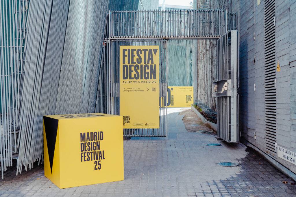 Una entrada al Festival de Diseño de Madrid con letreros amarillos sobre un fondo urbano.