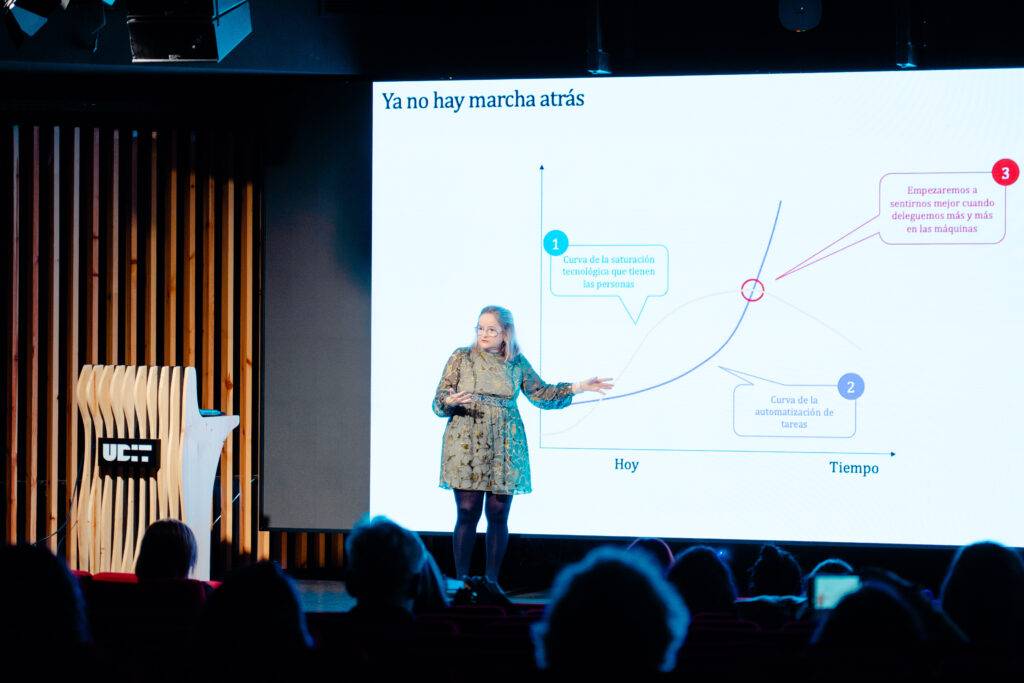 Una mujer presenta un gráfico durante una conferencia, mientras la audiencia observa atentamente.