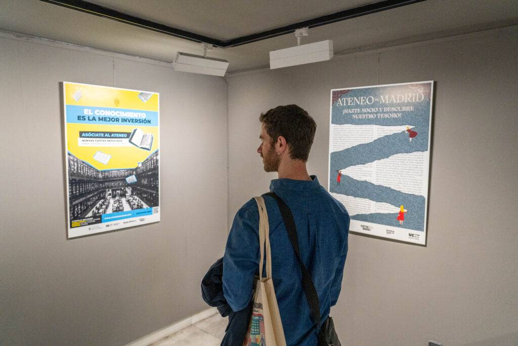 Un hombre observa atentamente dos carteles en una exposición.