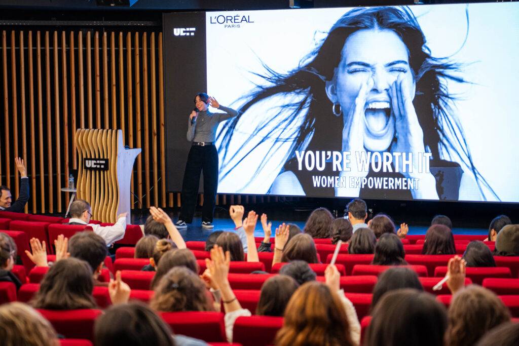 Una presentación sobre el empoderamiento femenino con un público entusiasta levantando las manos.