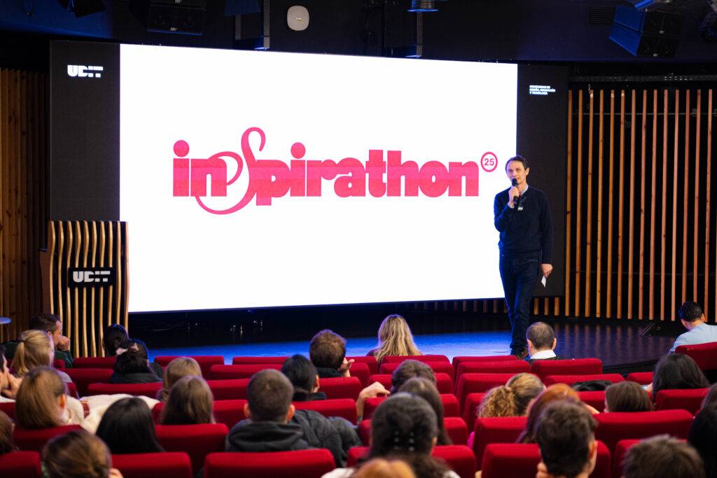 Un ponente habla frente a una audiencia en un evento llamado 'inspirathon'.