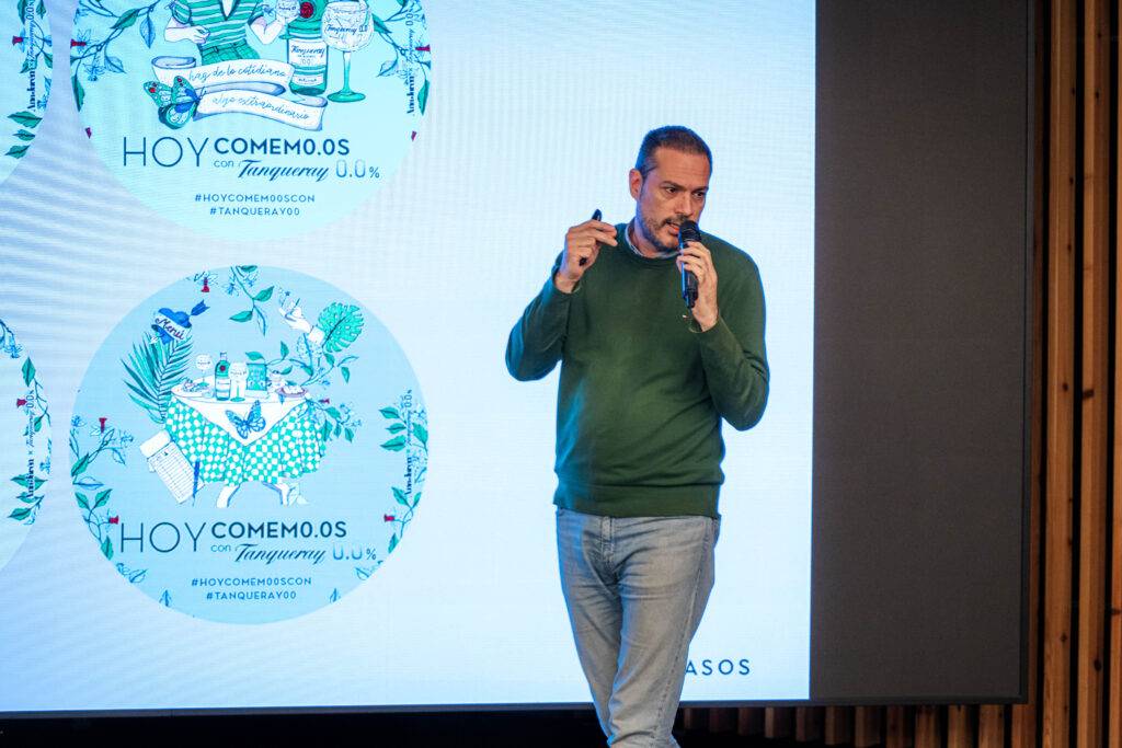 Un hombre con un suéter verde presenta en un evento frente a una pantalla con gráficos coloridos.