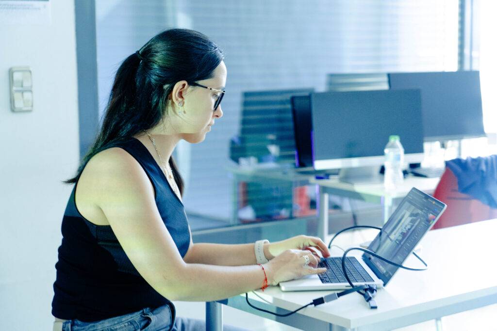 Una mujer trabaja en una computadora portátil en un entorno moderno y luminoso.