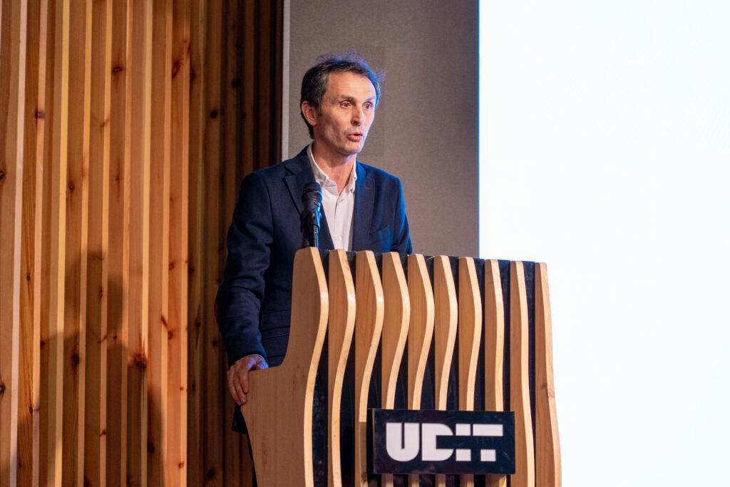 Un hombre de pie frente a un podio de madera, hablando en un evento.