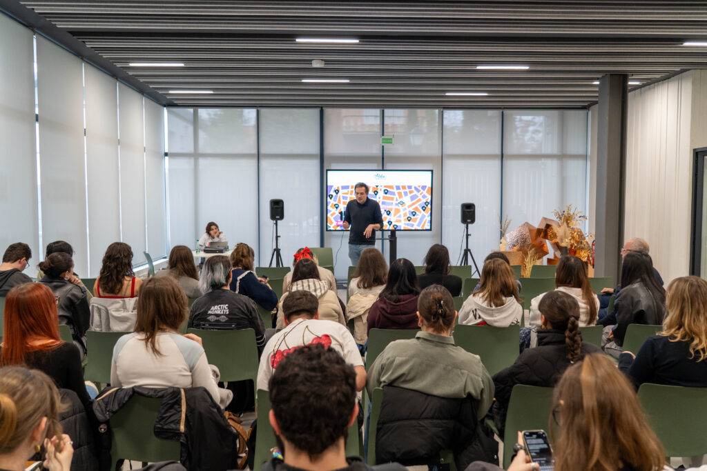 Una presentación en un aula con un orador frente a un grupo grande de personas sentadas.