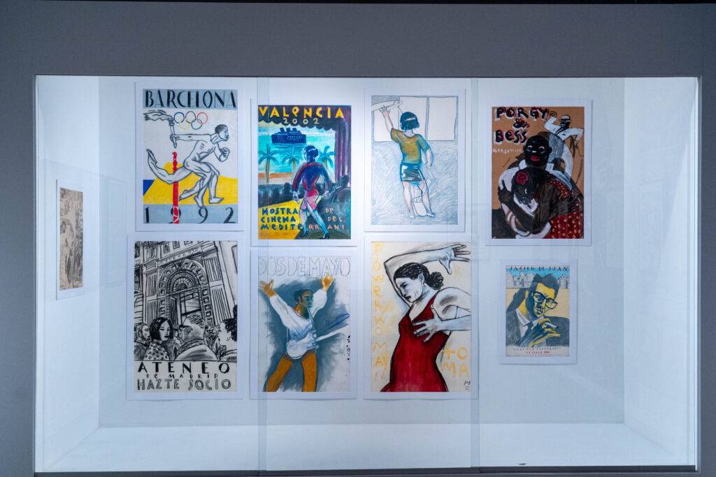 La imagen muestra una colección de carteles artísticos enmarcados en una vitrina, destacando diferentes estilos y temáticas visuales.