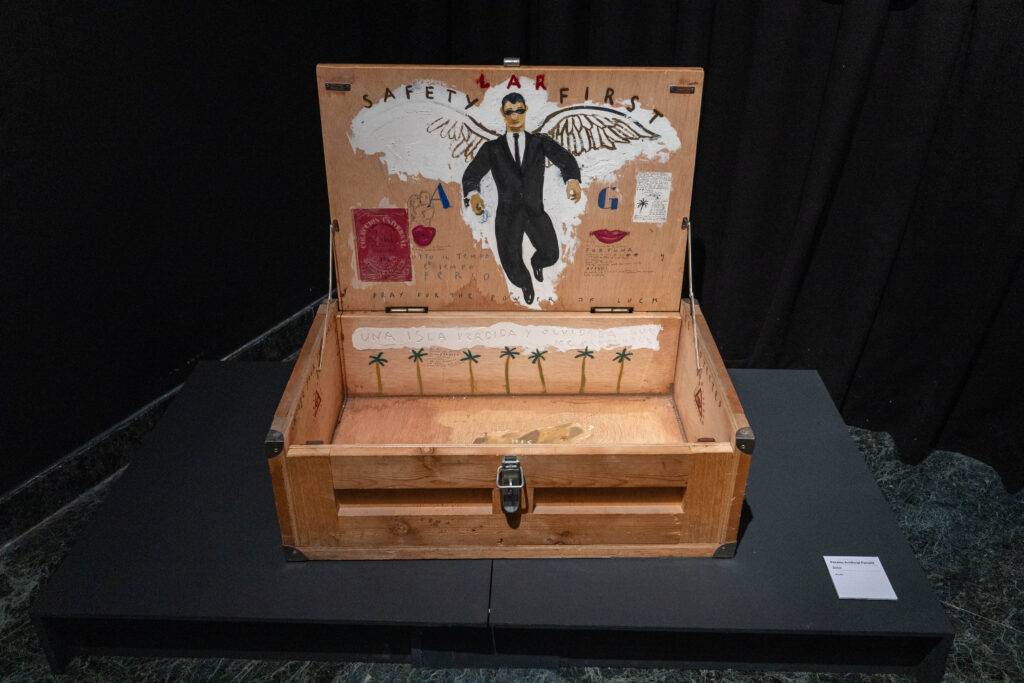 Una caja de madera abierta con una ilustración de un hombre con alas y varios elementos decorativos en su interior.
