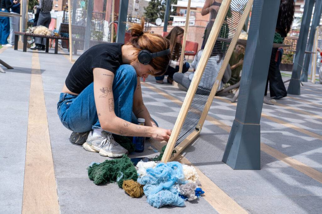Una mujer está trabajando en un telar, rodeada de hilos de lana de diferentes colores.