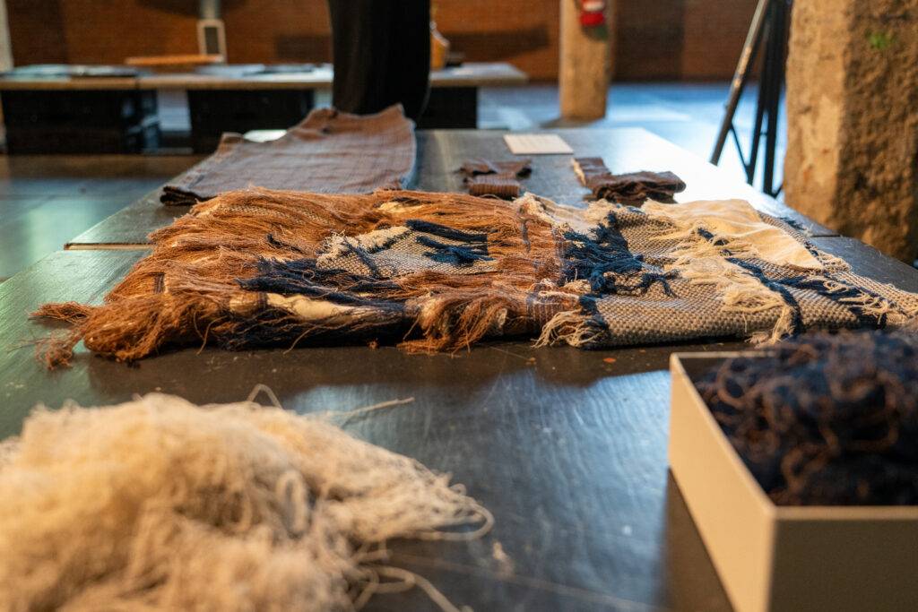 La imagen muestra una mesa con diversos tejidos y hilos de diferentes texturas y colores en un entorno artístico.