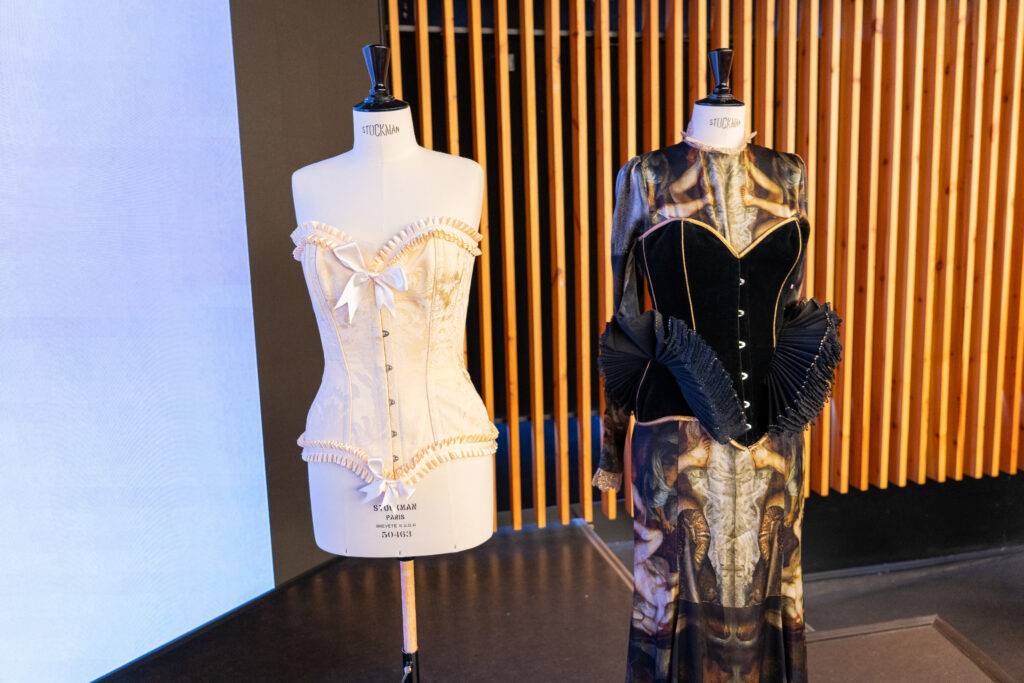 La imagen muestra dos maniquíes exhibiendo prendas de vestir, un corsé blanco y un vestido oscuro con detalles elaborados.