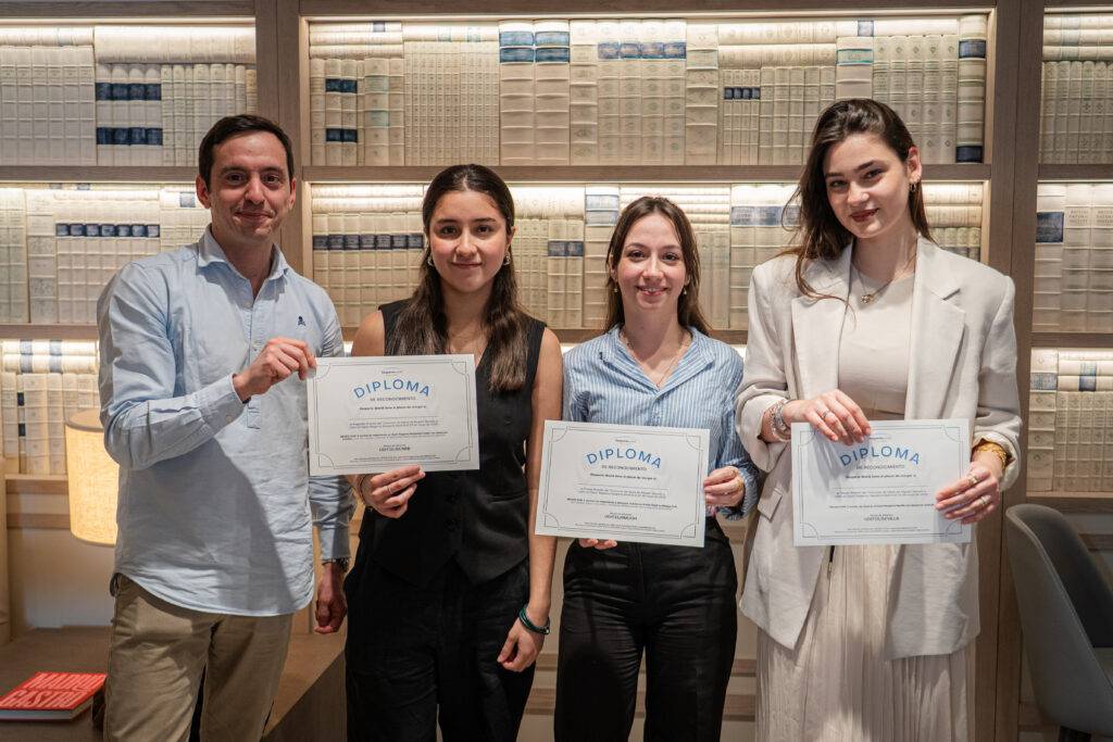 Cuatro personas sosteniendo diplomas en un ambiente académico.