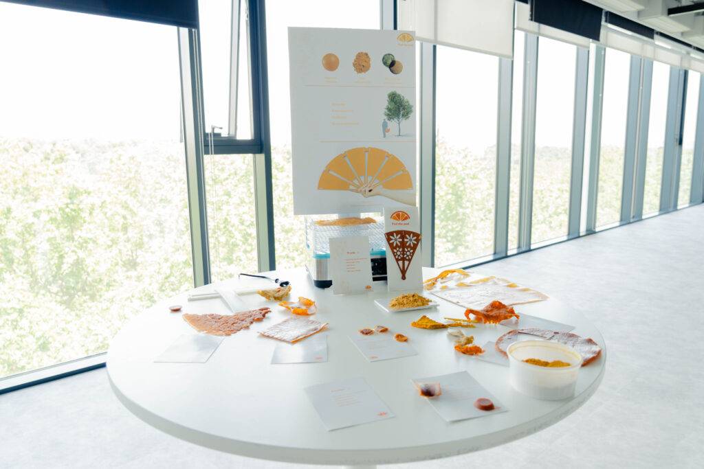 Una mesa presenta una exhibición sobre productos derivados de la naranja, con diversos elementos en un entorno luminoso.
