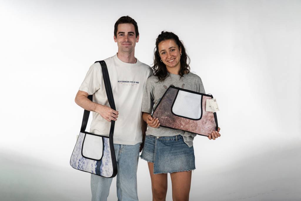 Dos personas posan sonrientes sosteniendo bolsas de diferentes colores.
