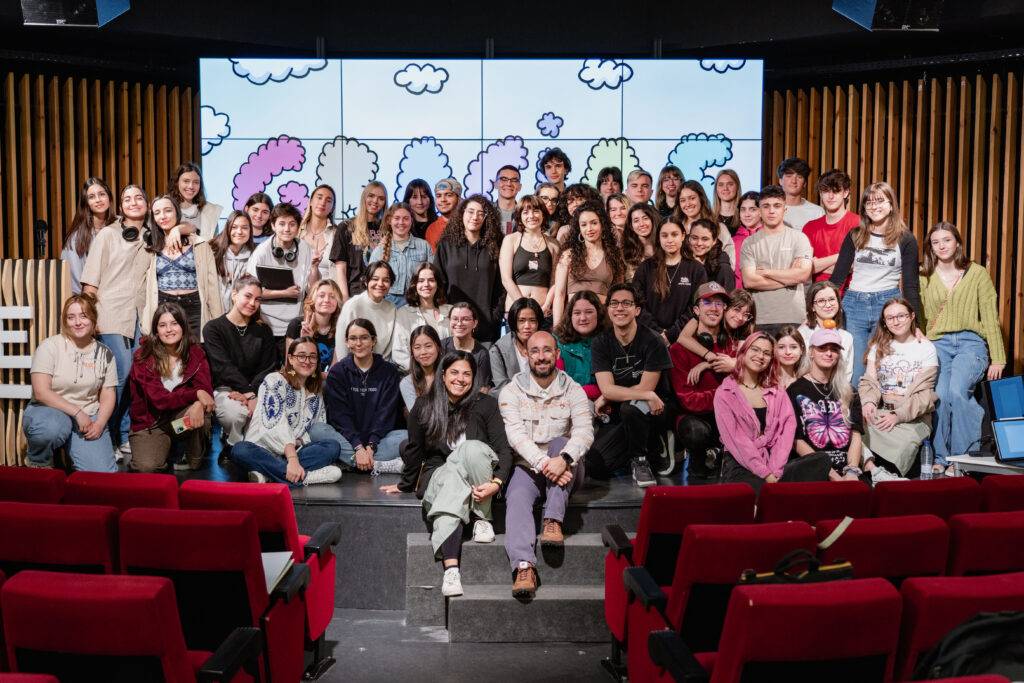 Un grupo grande de personas sonrientes posa para una foto en un evento, con un fondo colorido y acogedor.