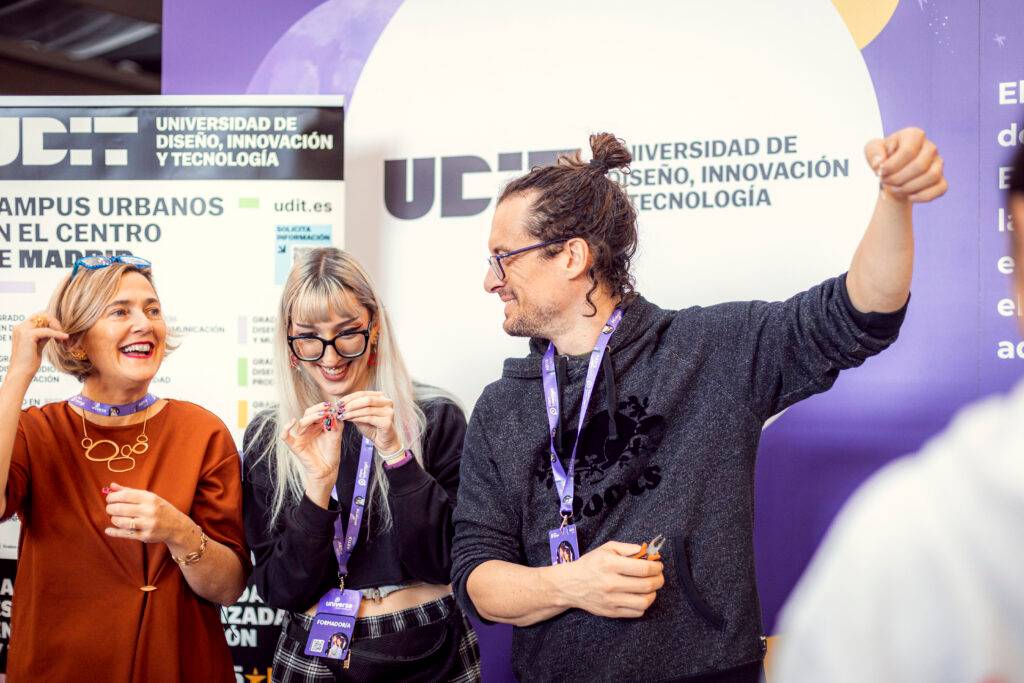 Un grupo de tres personas sonrientes interactuando en un evento relacionado con innovación y diseño.