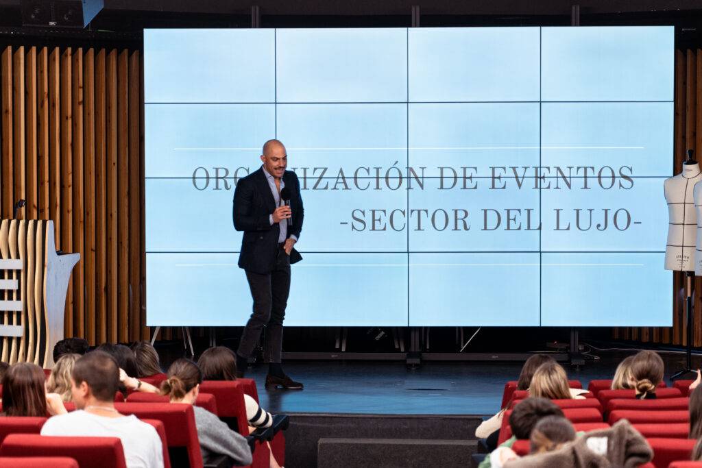 Un presentador habla sobre la organización de eventos en el sector del lujo frente a una audiencia sentada.