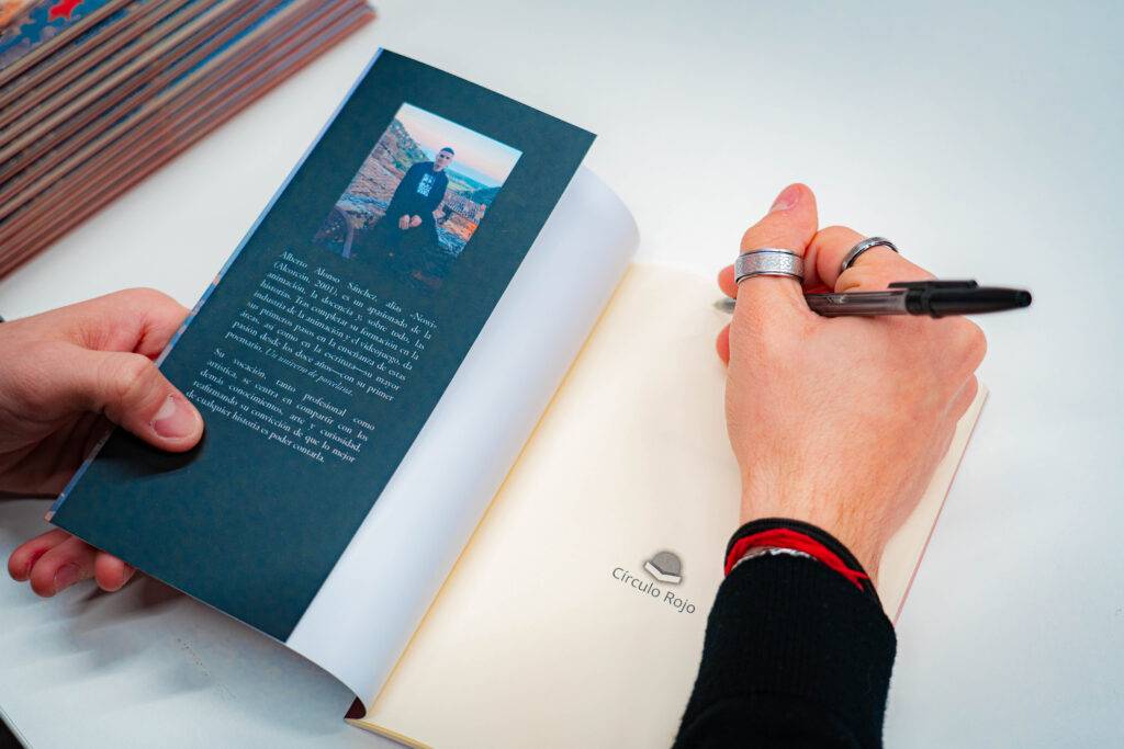 Una persona está firmando un libro abierto en una mesa.